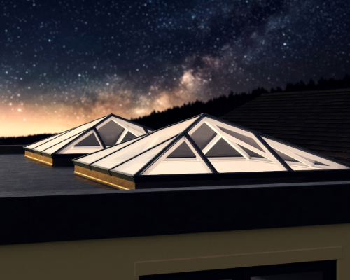 Illuminated glass roof lantern on a flat roof under a starry night sky.