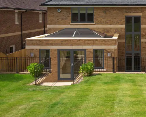 Modern brick house with a flat roof extension featuring a large glass roof lantern and patio doors opening to a green lawn.